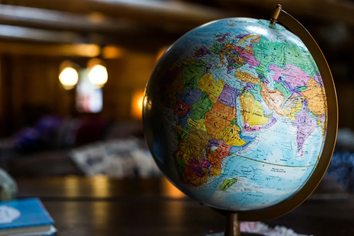 A colorful globe on a wooden table in a dimly lit room, with warm lights and blurred details in the background.