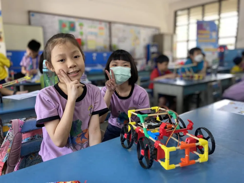 Girls smiling beside their handmade electric vehicle