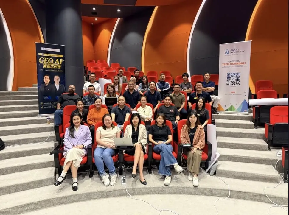 Group photo of the AI Forward CXO Masterclass cohort seated in the auditorium between the CEO AI workshop banner and the Agmo Academy tech trainings banner